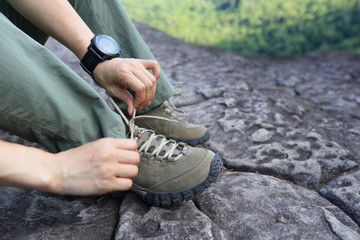 Young woman hiker tying shoelace on mountain peak