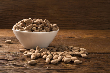 Almonds in white bowl on wooden background