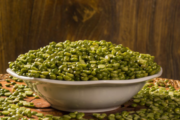 Green lentils inside a white pot on wood background. Edible raw pulses of the legume family.