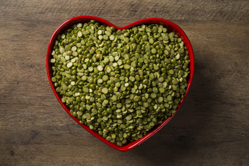 Green lentils inside a heart pot on wood background. Edible raw pulses of the legume family.