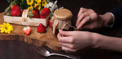Jelly strawberry on the wooden background with flowers. Female hands close to the bank.