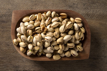 pistachio nuts in wood bowl with wood background.