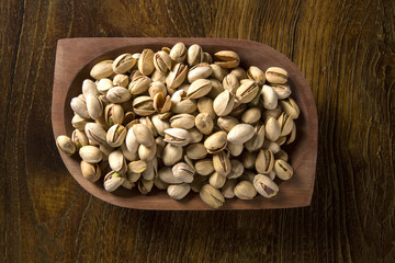 pistachio nuts in wood bowl with wood background.