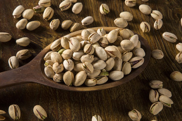 pistachio nuts in wood spoon on wood background