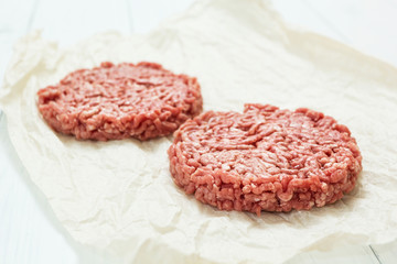 Raw hamburgers made from organic pork on a white wooden background.