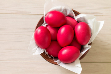 Ceramic bowl with red Easter eggs on wooden background. Aerial view.