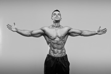 Black and white photo of Muscular and fit young fitness model posing over grey background.