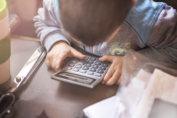 Cute little toddler boy using a calculator, figuring out a math problem, developing logic skills