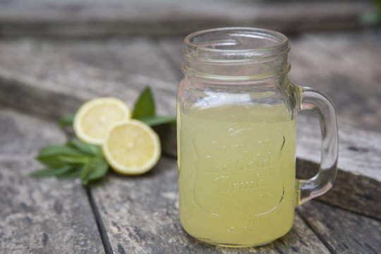 Lemon juice in jar, decorated with fresh lemons and mint leaves.