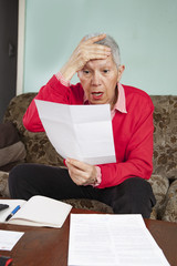 Senior old woman shocked with the bills she receives, appalled and gasping