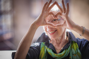 Cute senior old woman making a heart shape with her hands and fingers - obrazy, fototapety, plakaty