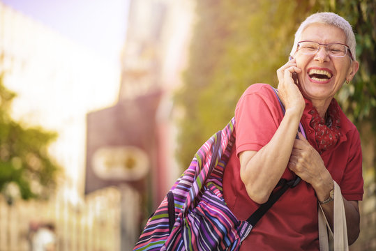 Senior Old Woman, A Tourist In A Foreign City, Talking On Her Phone With Her Family, Laughing Cheerfully