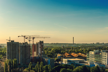 Urban scene with construction industry, cranes, building, houses, city skyline in sunset,