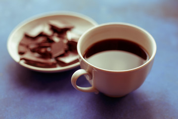 Cup of coffee and plate with chocolate on blue wooden table