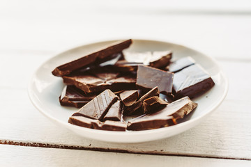 Broken bar of chocolate on plate on white wooden table