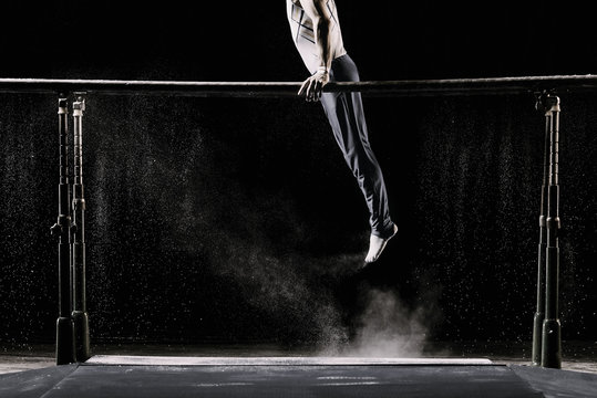 Male athlete performing handstand on gymnastic parallel bars with talcum powder. Isolated on black.