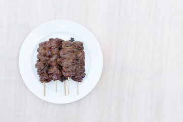 Grilled pork with bamboo stick in white dish on wooden background,Thai styled grill pork barbeque