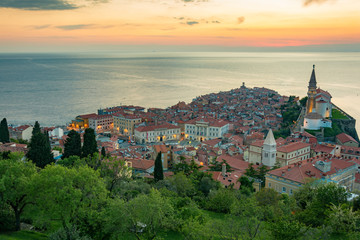 Fototapeta na wymiar View from the city walls of the church and town Piran as lights turn just little after the sunset