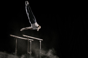 Male athlete performing difficult exercise on gymnastic parallel bars with talcum powder. Isolated...
