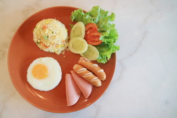 American style breakfast set American fried rice topped sunny up egg  sausage fried and slice tomato and cucumber.