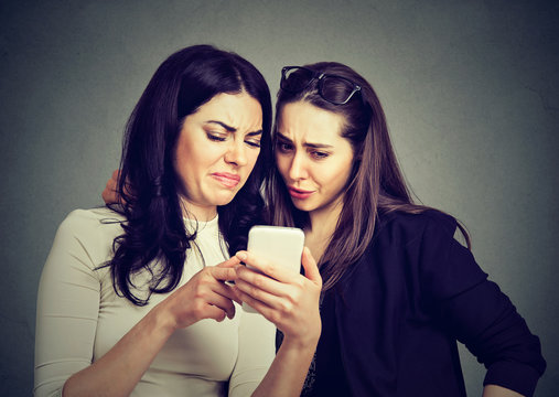 Two upset friends women viewing on line content on a smart phone