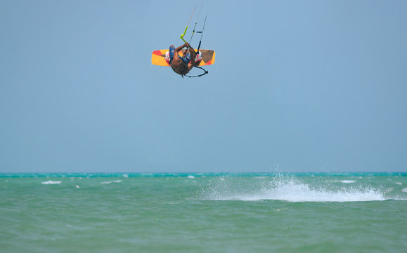 Professional kite boarding rider sportsman jumps high acrobatics kiteboarding trick with back rotation backroll from water. Recreational activity and extreme active water sports, hobby and fun time