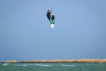 Professional kitesurfing rider sportsman jumps high acrobatics kiteboarding back mobe trick  with huge water splash. Recreational activity and extreme active water sports, hobby and fun in summer time