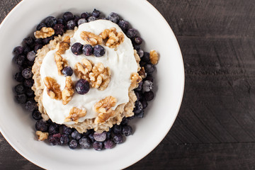  
Greek Vanilla Yogurt on a bed of oatmeal, Chia seeds, and frozen blueberries topped with walnuts top view
