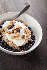  
Greek Vanilla Yogurt on a bed of oatmeal, Chia seeds, and frozen blueberries topped with walnuts on a dark wooden background
