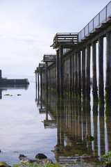 Colonnade wooden props pier with balconies and handrails covered green algae and reflected in water of Pacific Ocean