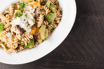  
Large White Bowl of cooked pasta topped with sundried tomatoes, bell peppers, broccoli, and parmesan cheese top view
