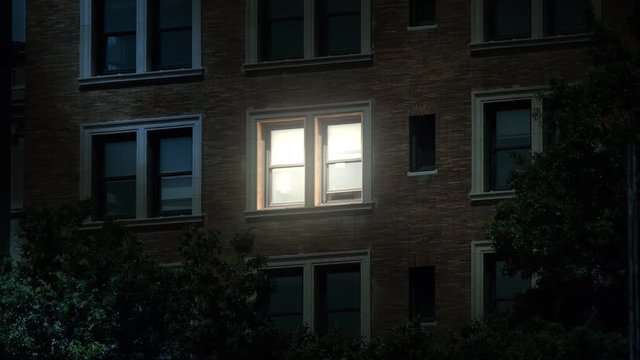A typical New York style apartment or office building establishing shot at night with the light from only one window on. Simulated "day-for-night" composite.	 	