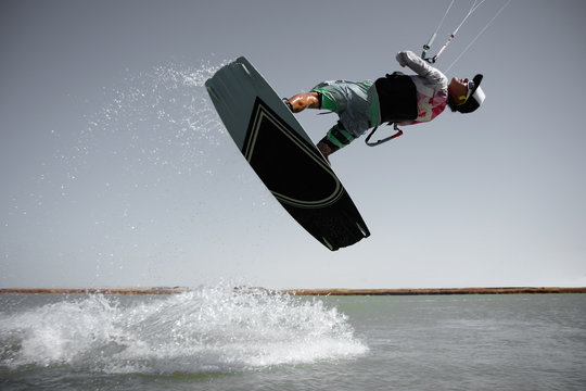 Professional kite boarding rider sportsman jumps high acrobatics kiteboarding front rotation trick tantrum with water splash. Recreational activity extreme active water sports