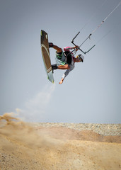 Kiter rides across the land. Professional kite boarding sportsman slides with board in desert sands and stones, extreme sport. Recreational activity and extreme active water sports, hobby and fun time
