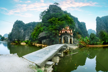 Outdoor park landscape with stone bridge and lake. Gate entrance to old Bich Dong pagoda complex. Ninh Binh, Vietnam - travel destination.