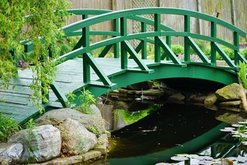 A green Japanese arch bridge in a garden 