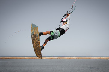 Professional kitesurfer  rider sportsman jumps high acrobatics kiteboarding trick with front rotation from sand into water. Recreational activity and extreme active water sports, hobby and fun time