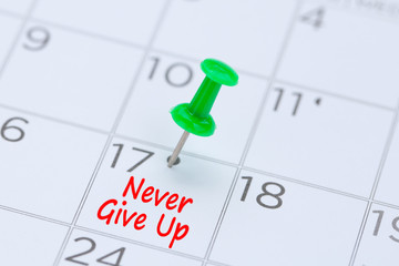 Never give up written on  a calendar with a green push pin to remind you and important appointment.