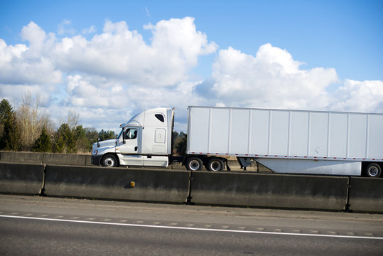 Excellent modern white semi truck trailer dry van on highway with concrete border and cloud sky side view