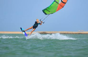 Kite surfing girl in sexy swimsuit with kite in sky on kiteboard in the blue sea jumping kiteboarding trick. Recreational activity, water sports, action, hobby, fun in summer time. Kiteboarding sport
