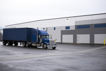 Blue classic semi truck with container on warehouse buildings place