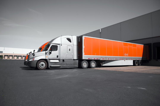 Bright modern orange and gray semi trucks unloading in warehouse