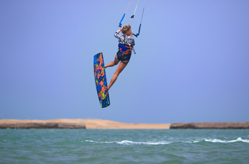 Kitesurfing girl in sexy swimsuit with kite in blue sky on kiteboard in the blue sea jumping air trick. Recreational activity, water sports, action, hobby and fun in summer time. Kiteboarding sport
