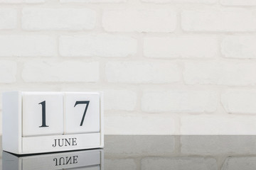 Closeup white wooden calendar with black 17 june word on black glass table and white brick wall textured background with copy space , selective focus at the calendar
