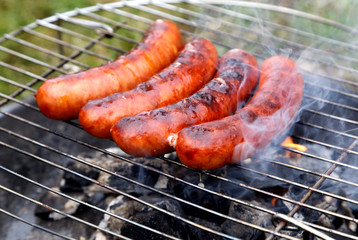  Four grilling sausages on barbecue grill. Selective focus