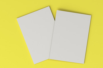 Two blank white closed brochure mock-up on yellow background