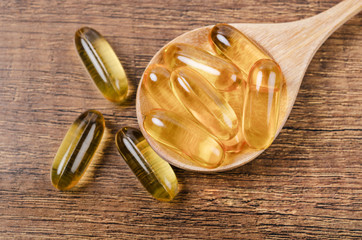 Fish oil capsules with omega 3 and vitamin D in a wooden spoon.