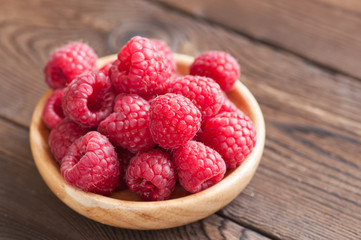Close up of heap of ripe red sweet raspberries in a wooden plate. Wooden background.