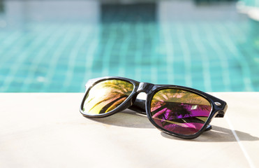 Design sunglasses on swimming pool edge, summer concept background, outdoor day light