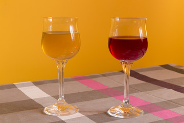 Two crystal glasses with red and white wine on the table on yellow background